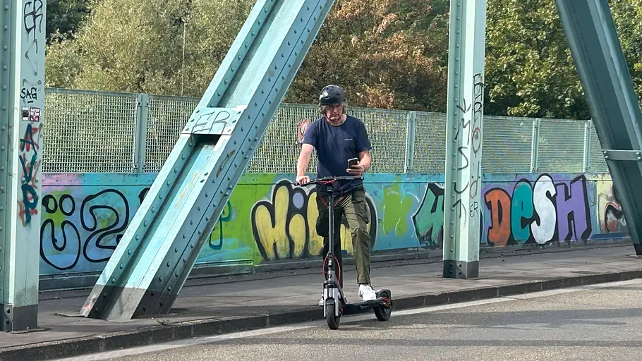 E-Scooter Segway Ninebot F3 Pro D Die Außenaufnahme zeigt einen Testredakteur auf dem stehenden E-Scooter Segway Ninebot F3 Pro D beim Blick auf sein Mobiltelefon.