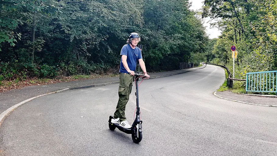 E-Scooter Segway Ninebot F3 Pro D Die Außenaufnahme zeigt einen Testredakteur auf dem E-Scooter Segway Ninebot F3 Pro D beim Bergauffahren durch eine Kurve.