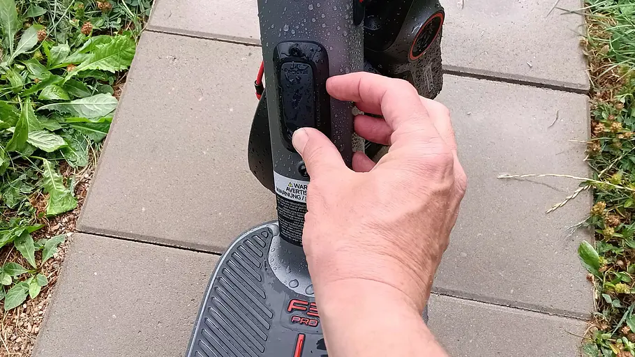 E-Scooter Segway Ninebot F3 Pro D Die Detailaufnahme zeigt die Hand eines Testredakteurs beim Öffnen der Ladeklappe des Segway Ninebot F3 Pro D.