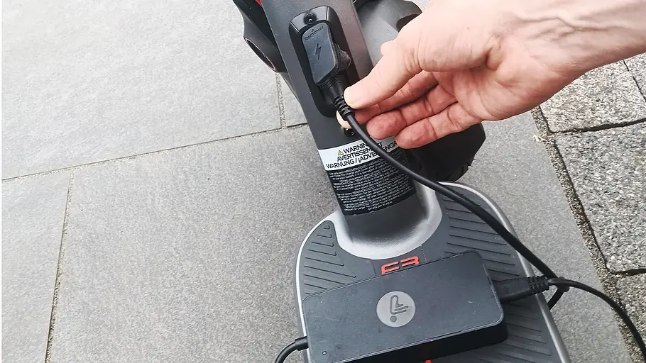 E-Scooter Segway Ninebot F3 Pro D Die Detailaufnahme zeigt die Hand eines Testredakteurs beim Einstecken des Ladsteckers des Segway Ninebot F3 Pro D.