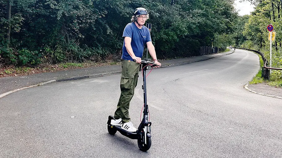 E-Scooter Segway Ninebot F3 Pro D Die Außenaufnahme zeigt einen Testredakteur auf dem E-Scooter Segway Ninebot F3 Pro D beim Bergauffahren durch eine Kurve.