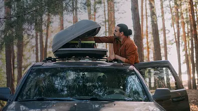 Mann öffnet Dachbox eines im Wald stehenden Autos. - Foto: eBay