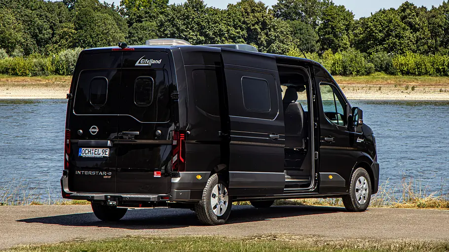 Der Eifelland Nissan Interstar-e an einem Flussufer stehend mit geöffneter Schiebetüre von schräg hinten rechts.