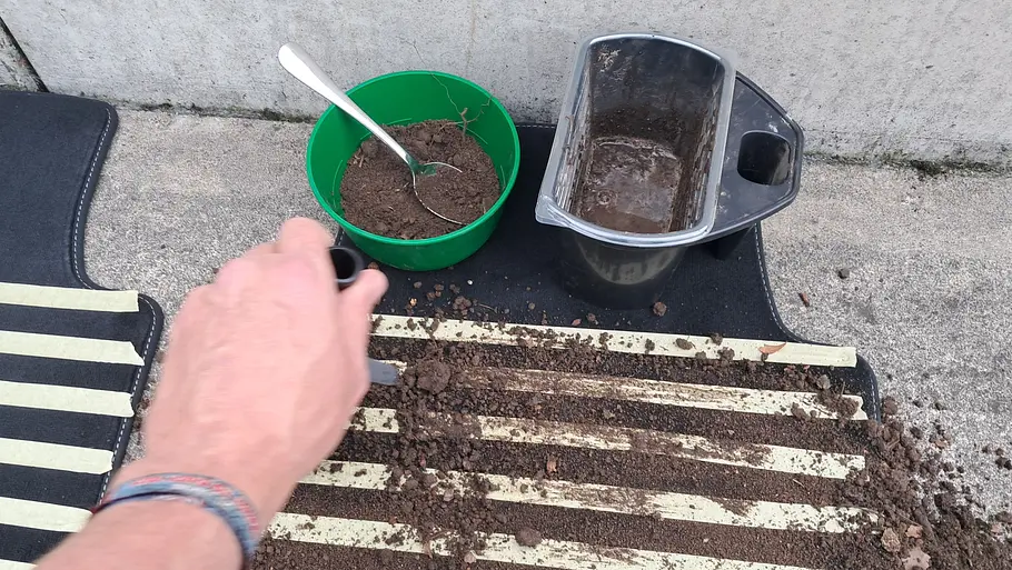Testschmutz (Blumenerde) wird per Pinsel auf eine Fußmatte aufgetragen.