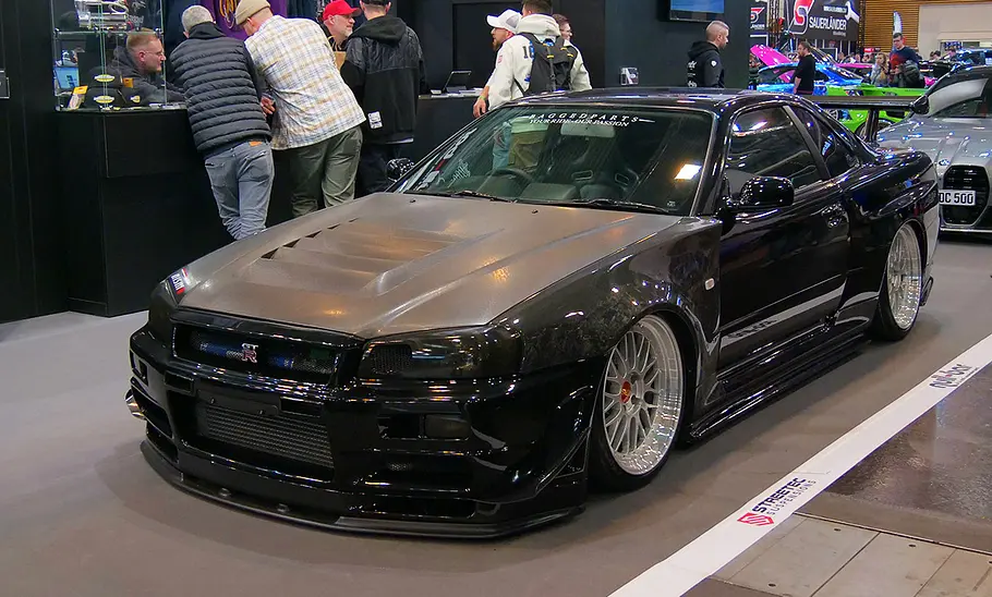 Der Nissan Skyline R34 GT-R mit Carbon-Tuning auf der Essen Motor Show 2024 von schräg vorne fotografiert.
