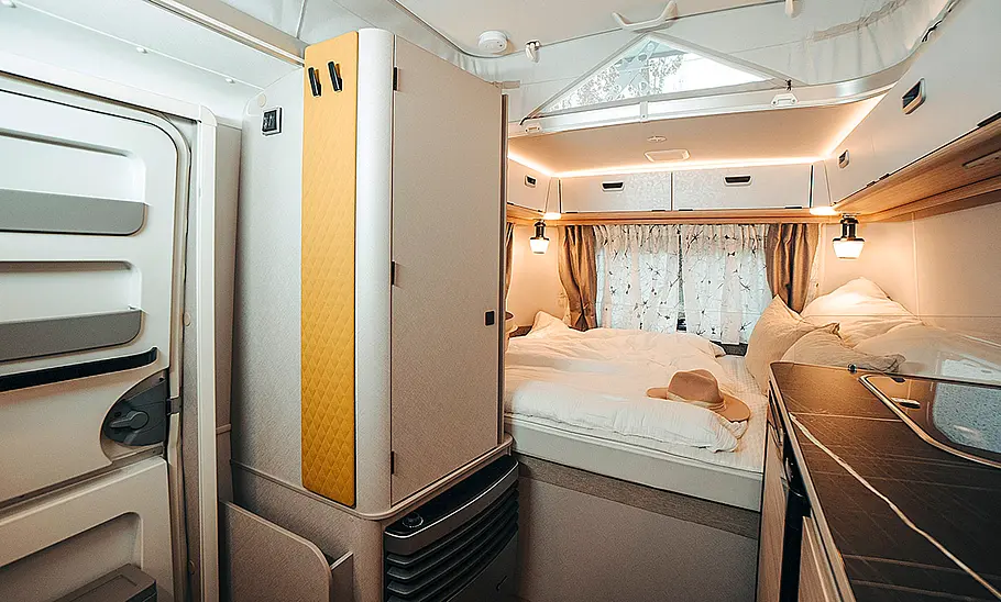Das Bild zeigt den Heckbereich des Wohnraums des Eriba Touring 310 (2025) mit Kleiderschrank links, Bett in der Mitte und Küchenzeile rechts.