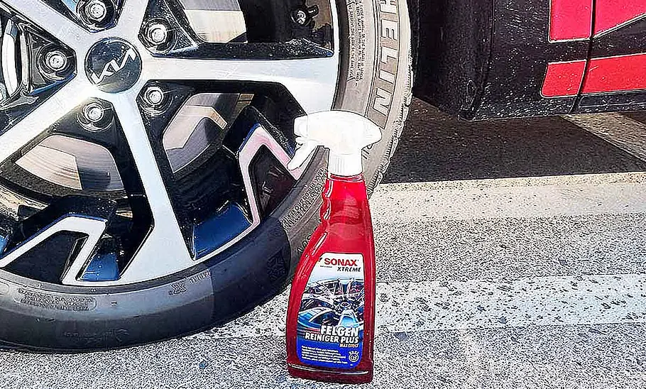 Eine Flasche Sonax Xtreme Felgenreiniger Plus steht vor einer Autofelge.