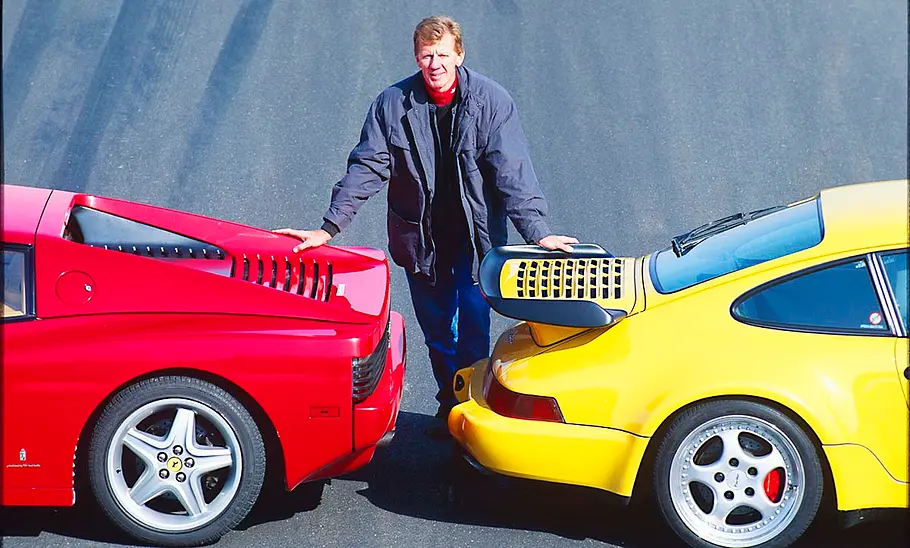 Walter Röhrl steht zwischen Ferrari 512 TR und Porsche 911 Turbo
