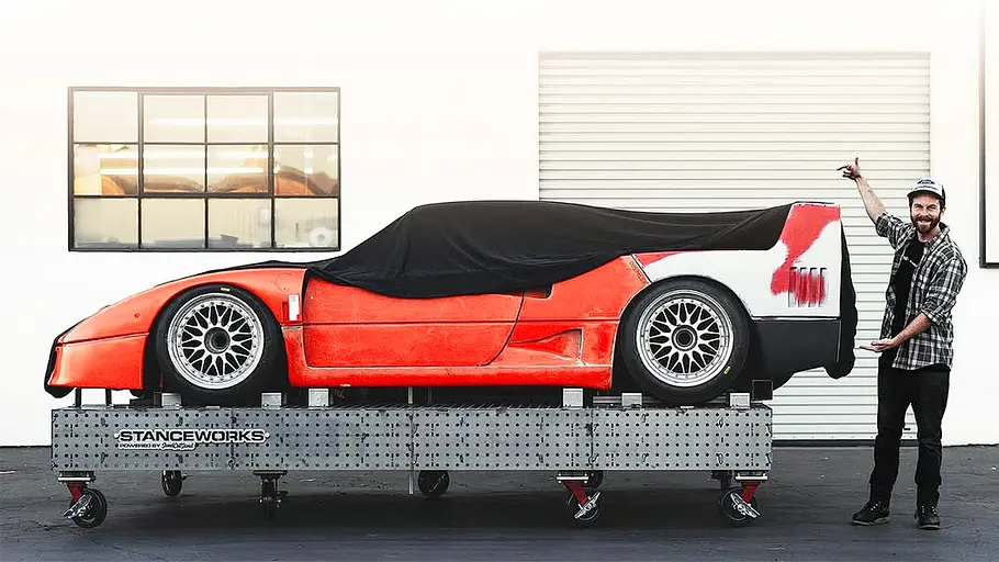 Blick von der Seite auf einen Ferrari F40, der noch teilweise durch ein dunkles Tuch verdeckt ist.