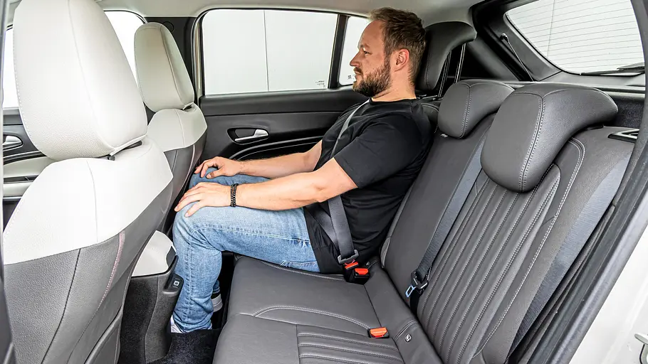 Mann sitzt im Fond des Fiat 600e, Blick auf Beinfreiheit und Rücksitzbank in Grau