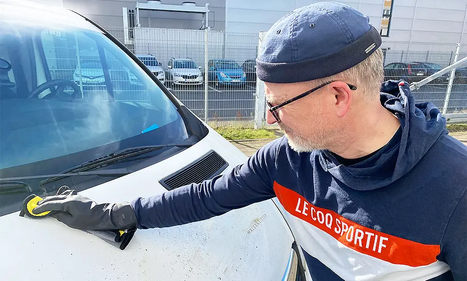 Ein Testredakteur wischt mit einem Poliertuch Radiererreste von der Motorhaube des Testfahrzeugs.