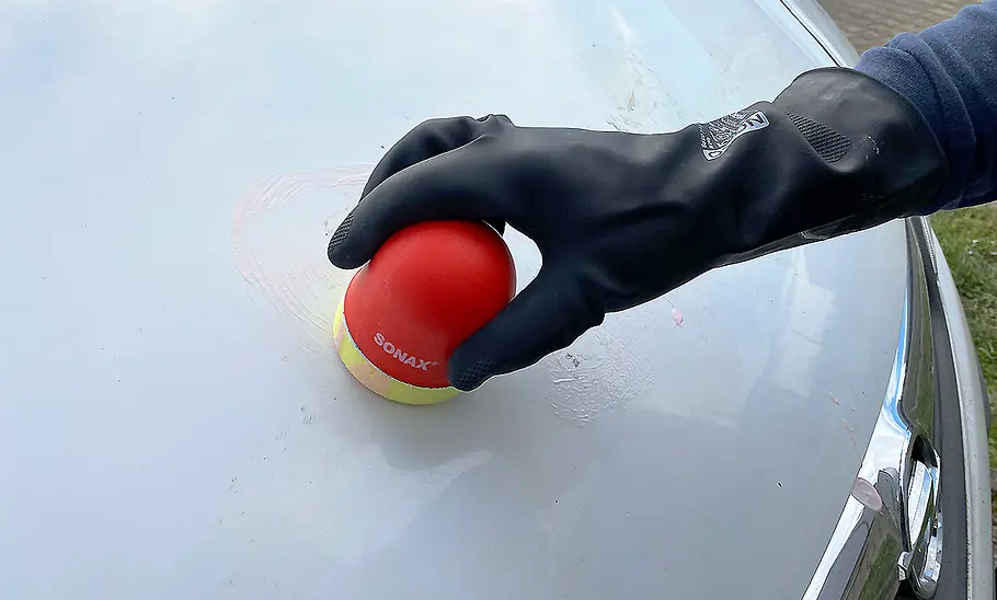 Hand mit Gummihandschuh beim Polieren der Motorhaube.