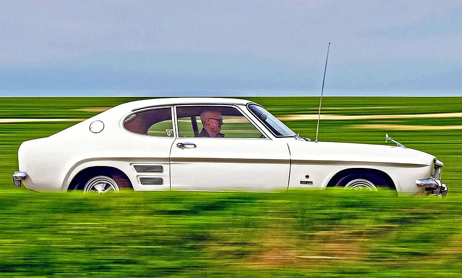 Der Ford Capri fährt auf einer Landstraße, Ansicht von der rechten Seite.