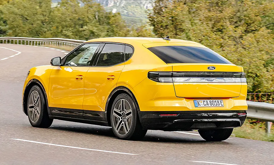 Ford Capri (2024) Der Ford Capri (2024) bei der Fahrt über eine kurvige Landstraße; von schräg hinten fotografiert.