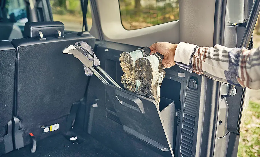 Eine Person zieht ein Paar Schuhe aus einem Staufach im Laderaum des Ford E-Tourneo Courier (2025).