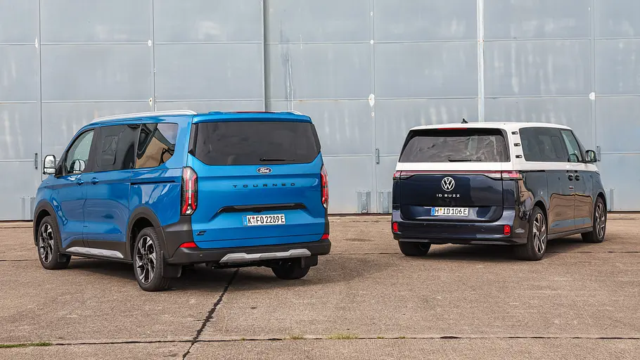 Ford E-Tourneo Custom und VW ID. Buzz LWB stehen auf einem Parkplatz nebeneinander, von hinten fotografiert.