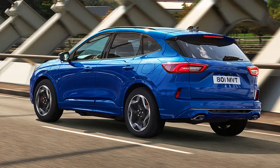Das Ford Kuga Facelift (2024) fährt durch eine Stadt, von hinten links fotografiert.