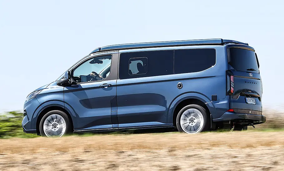 Ford Nugget (2024) Der Ford Nugget (2024) fahrend von schräg hinten fotografiert.