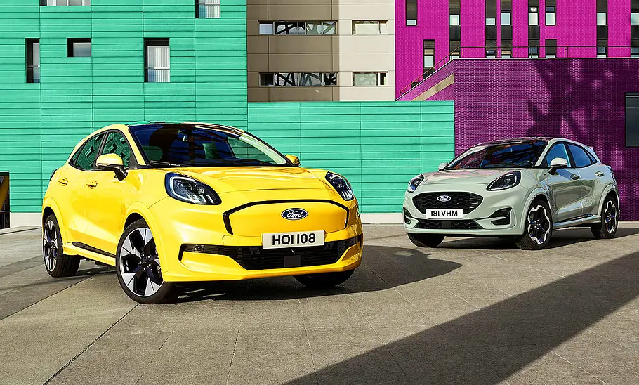 Der Ford Puma Gen-E (2025) statisch, von schräg vorne fotografiert um Vordergrund. Dahinter ein Ford Puma mit Verbrenner.