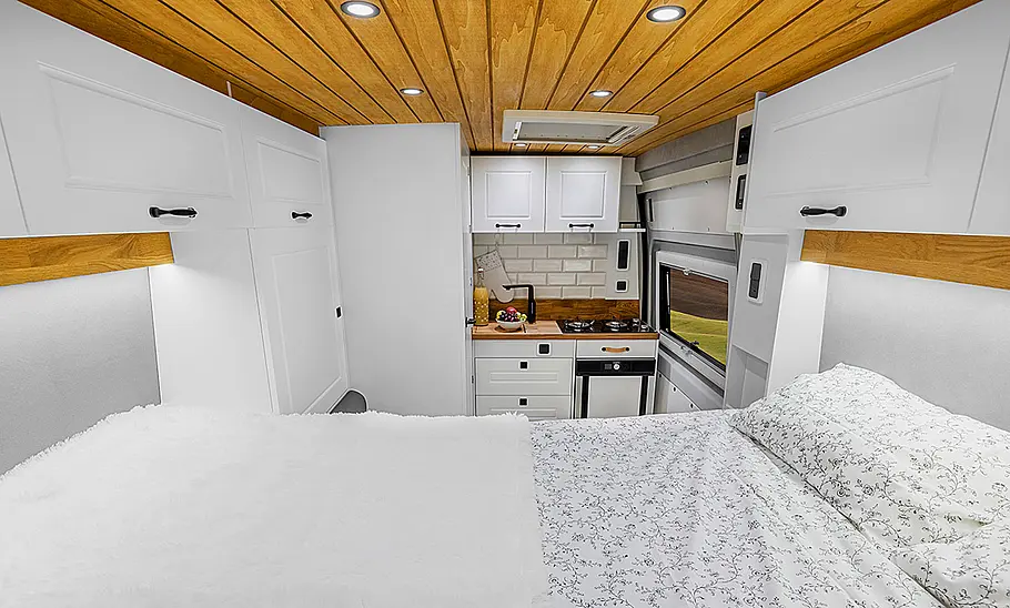 Das Bild zeigt den Wohnraum des Freedo RV 541 HT (2025) mit vollständig aufgebautem Heckbett und Blick in Richtung Fahrzeugfront.