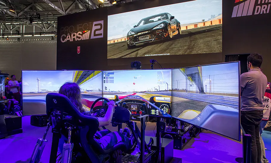 Spielende auf der Gamescom Bild zeigt Person auf einem Racing Rig und vor diversen Bildschirmen, die ein Rennspiel spielt.