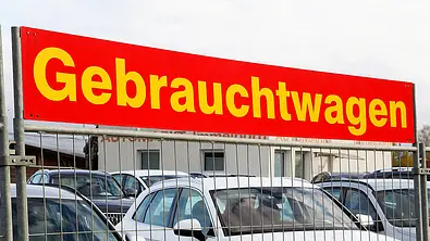 Ein Schild mit Gebrauchtwagen, darunter sieht man mehrere Fahrzeuge hinter einem Zaun. - Foto: Imago