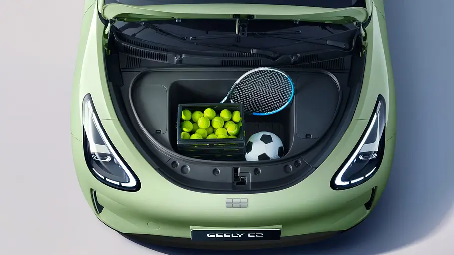 Der Frunk des Geely E2 unter der geöffneten Motorhaube aus der Draufsicht, beladen mit einer Box Tennisbälle, einem Tennisschläger und einem Fußball.