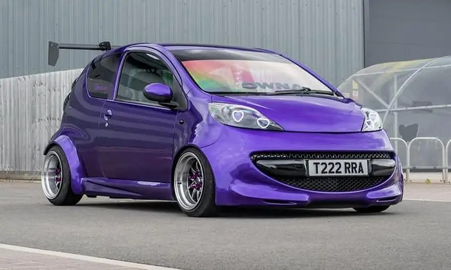 Peugeot 107 mit Widebody-Kit Der Peugeot 107 mit Widebody-Kit steht auf einem Platz und wurde von schräg vorne fotografiert.