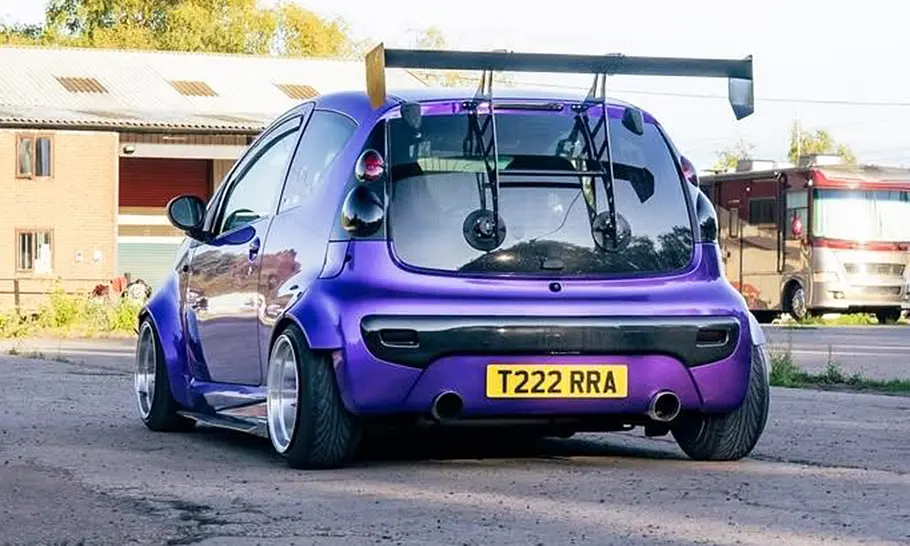 Peugeot 107 mit Widebody-Kit Der Peugeot 107 mit Widebody-Kit steht auf einem Platz und wurde von schräg hinten fotografiert.