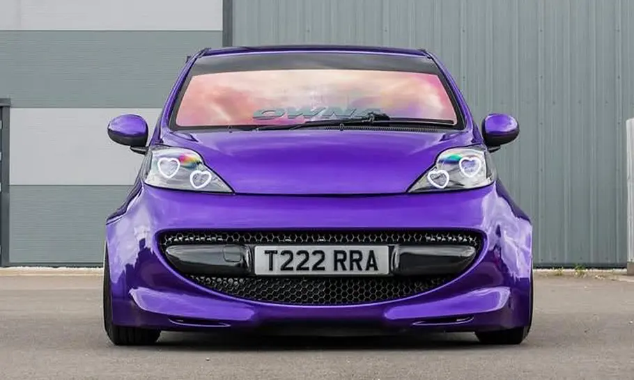 Peugeot 107 mit Widebody-Kit Der Peugeot 107 mit Widebody-Kit steht auf einem Platz und wurde von vorne fotografiert.