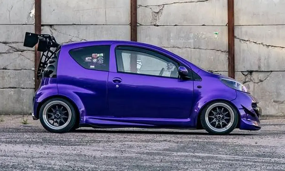 Peugeot 107 mit Widebody-Kit Der Peugeot 107 mit Widebody-Kit steht auf einem Platz und wurde von der Seite fotografiert.