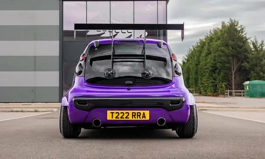 Peugeot 107 mit Widebody-Kit Der Peugeot 107 mit Widebody-Kit steht auf einem Platz und wurde von hinten fotografiert.