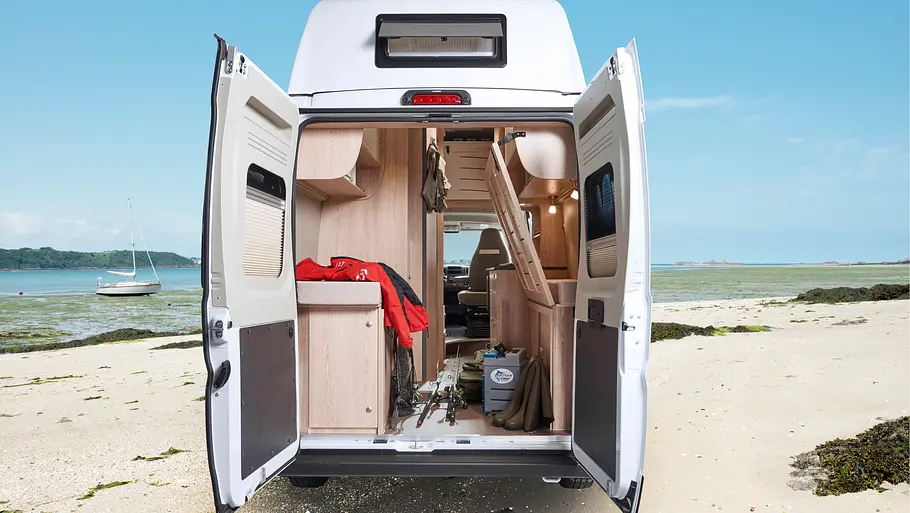 Blick durch die geöffneten Hecktüren in die Heckgarage des Globecar Globescout Vario mit seitlich hochgeklapptem Bett.