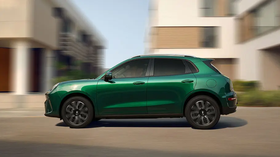 GWM-Ora-5-Hybrid-Fahrbericht Ein Ora 5 Hybrid in Grün fährt von der Seite betrachtet vor einem Haus entlang.