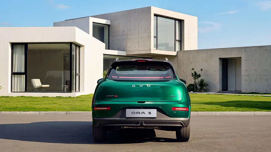 GWM-Ora-5-Hybrid-Fahrbericht Ein Ora 5 Hybrid in Grün steht von hinten betrachtet vor einem Haus.