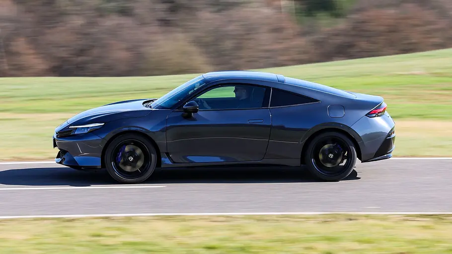Der Honda Prelude fährt auf einer Landstraße zwischen zwei Wiesen, von links fotografiert.