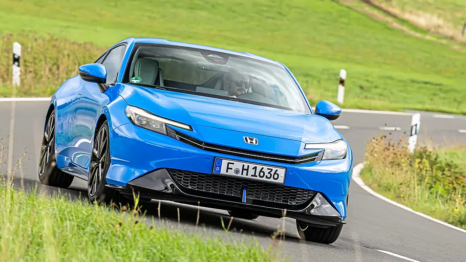 BMW 2er Coupé gegen Honda Prelude im Vergleichstest Ein blauer Honda Prelude fährt durch eine Kurve auf einer Landstraße, umgeben von grünen Wiesen. Am Steuer sitzt eine Person.