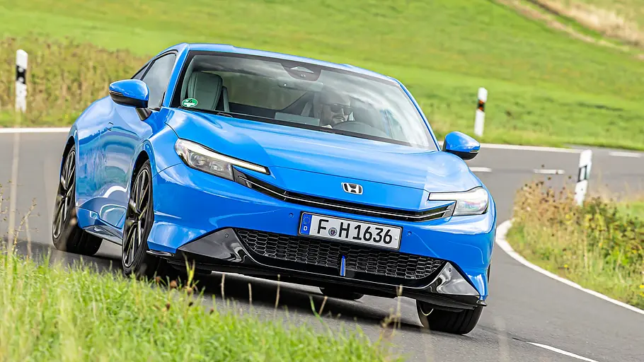 BMW 2er Coupé gegen Honda Prelude im Vergleichstest Ein blauer Honda Prelude fährt auf einer kurvigen Landstraße durch grüne Wiesen, schräg von vorn gesehen.