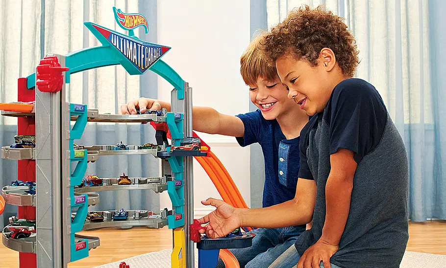 Zwei Kinder spielen mit einem Spielzeug-Parkhaus von Hot Wheels.