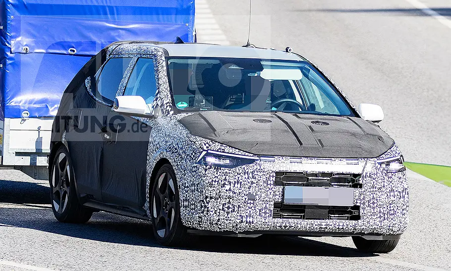 Blick von schräg vorne auf den fahrenden Erlkönig des Hyundai i20 (2026), der einen Anhänger zieht.