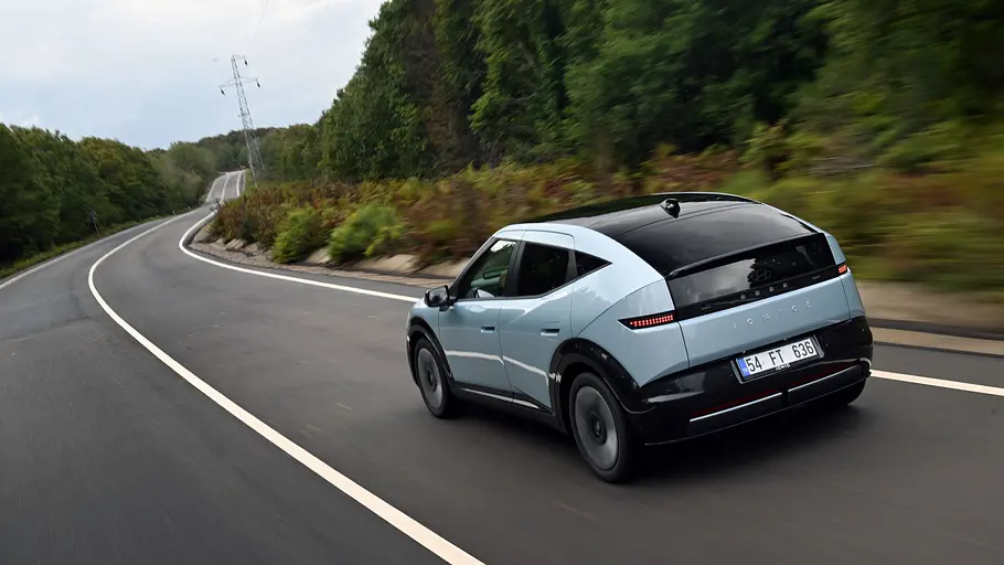 Ein blauer Hyundai Ioniq 3 von schräg hinten, fahrend auf einer Landstraße