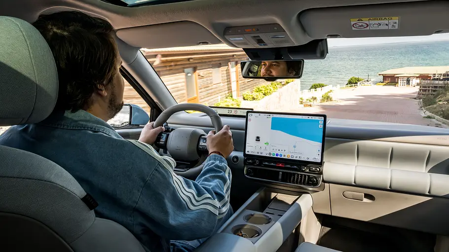 Das Cockpit des Hyundai Ioniq 3 mit dem Autoren dieses Artikels am Steuer, fotografiert von den Rücksitzen