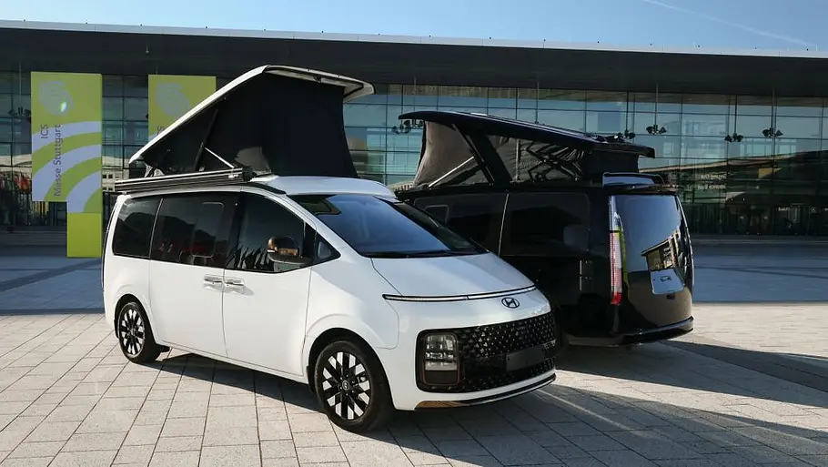 Hyundai Staria Camper Concept Zwei Hyundai Staria Camper-Concept nebeneinander stehend vor der Messe Stuttgart. Das weiße Fahrzeug ist von schräg vorne rechts zu sehen, das schwarze Fahrzeug parallel dazu von hinten links.