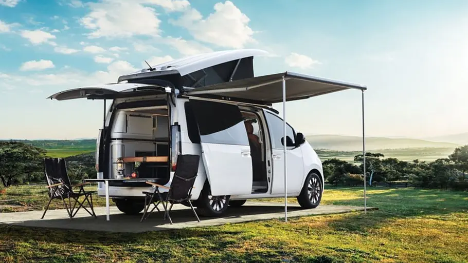Das Hyundai Staria Camper-Concept statisch von schräg hinten rechts mit geöffneter Heckklappe, Schiebetüre, Markise und Aufstelldach.