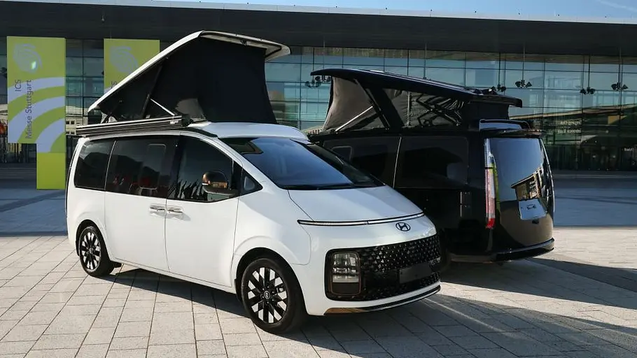Hyundai Staria Camper Concept Zwei Hyundai Staria Camper-Concept nebeneinander stehend vor der Messe Stuttgart. Das weiße Fahrzeug ist von schräg vorne rechts zu sehen, das schwarze Fahrzeug parallel dazu von hinten links.