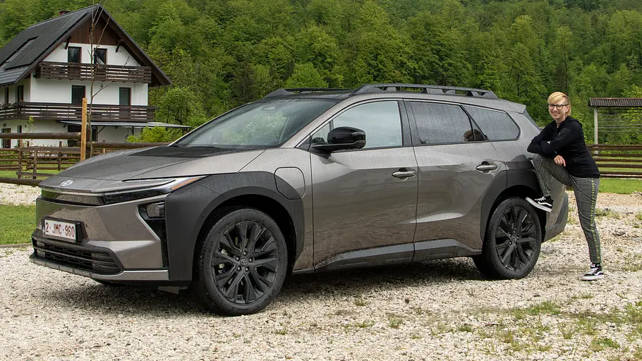 Toyota bZ4X Touring AWD stehend von der Seite. Eine Person steht mit einem Fuß auf dem Hinterrad aufgestützt am Heck...