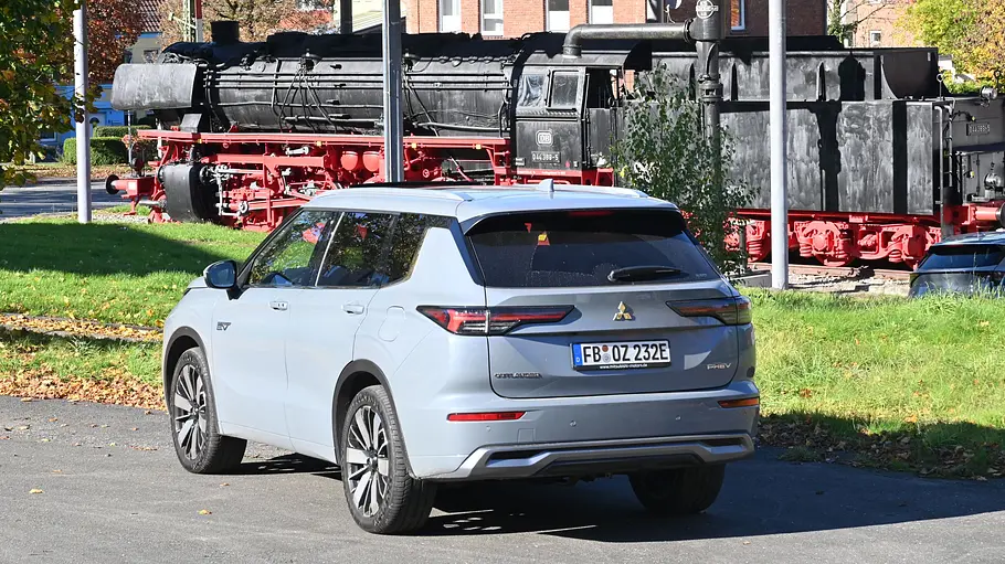 Der Mitsubishi Outlander steht vor einer alten Dampflokomotive, fotografiert von schräg hinten.