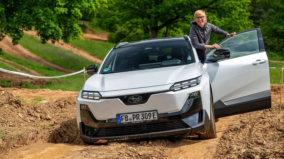 Subaru Uncharted (2026) mit Allradantrieb auf einer Matschpiste, Ansicht von vorne. In der geöffneten linken Tür steht eine Person.