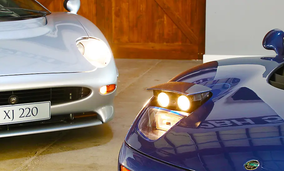 Der Jaguar XJ220 und Jaguar XJR-15 statisch mit eingeschalteten Scheinwerfern von schräg vorne fotografiert.
