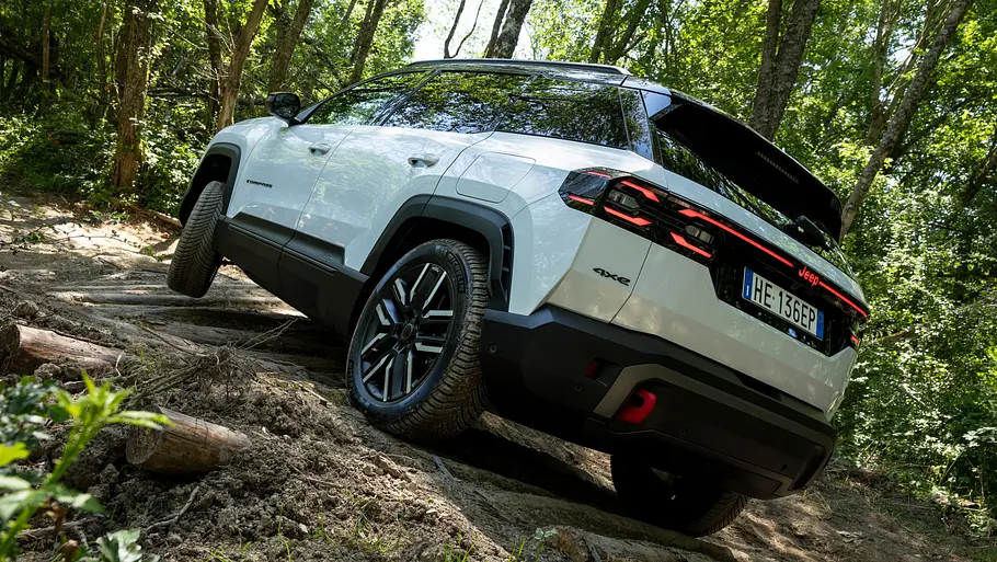 Der Jeep Compass 4xe Elektro fährt im Gelände einen Hang hinauf, von hinten links fotografiert.